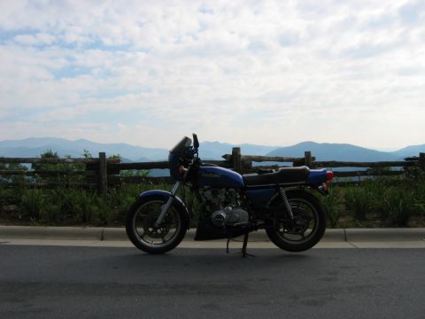1985 Ford LTD Crown Victoria - A blue Suzuki motorcycle is parked on the roadside with a scenic mountain view.