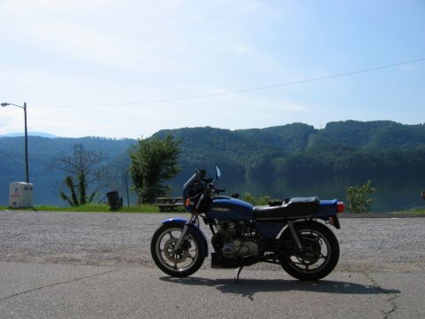 1985 Ford LTD Crown Victoria - Blue Suzuki motorcycle parked at a scenic overlook with a lake and forested mountains.