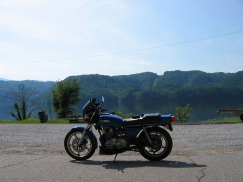 1985 Ford LTD Crown Victoria - A blue Suzuki motorcycle is parked on the side of the road with a scenic view of a lake and mountains.