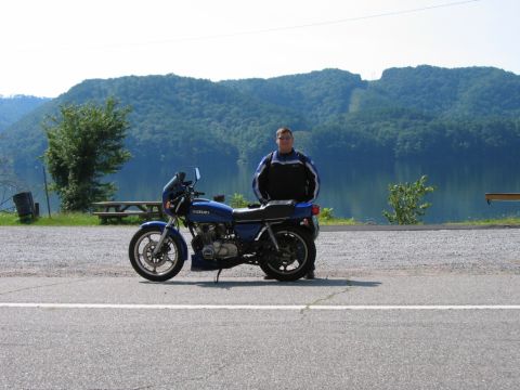 1985 Ford LTD Crown Victoria - A rider poses with a blue Suzuki motorcycle by a lake.