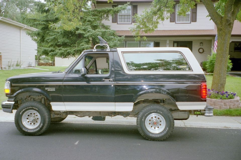Side view of a black and white 1993 Ford Bronco with a roof rack and aftermarket wheels