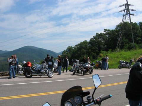 1985 Ford LTD Crown Victoria - A group of motorcyclists gathered on a scenic roadside, with a power line tower visible against the mountains.