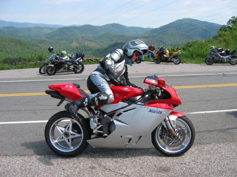 1985 Ford LTD Crown Victoria - A rider on a red and silver MV Agusta motorcycle pauses on a scenic road with other motorcycles in the background.