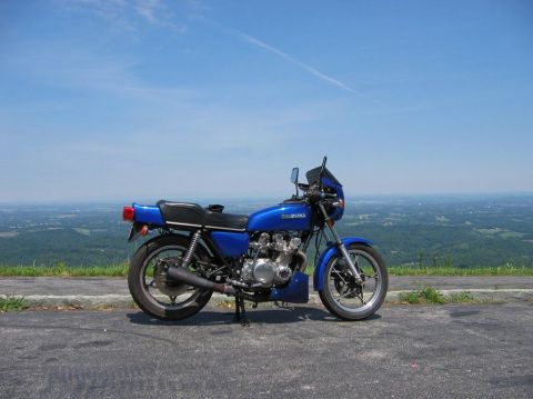 1985 Ford LTD Crown Victoria - A blue Suzuki motorcycle is parked on an asphalt surface with a scenic overlook in the background under a clear blue sky.