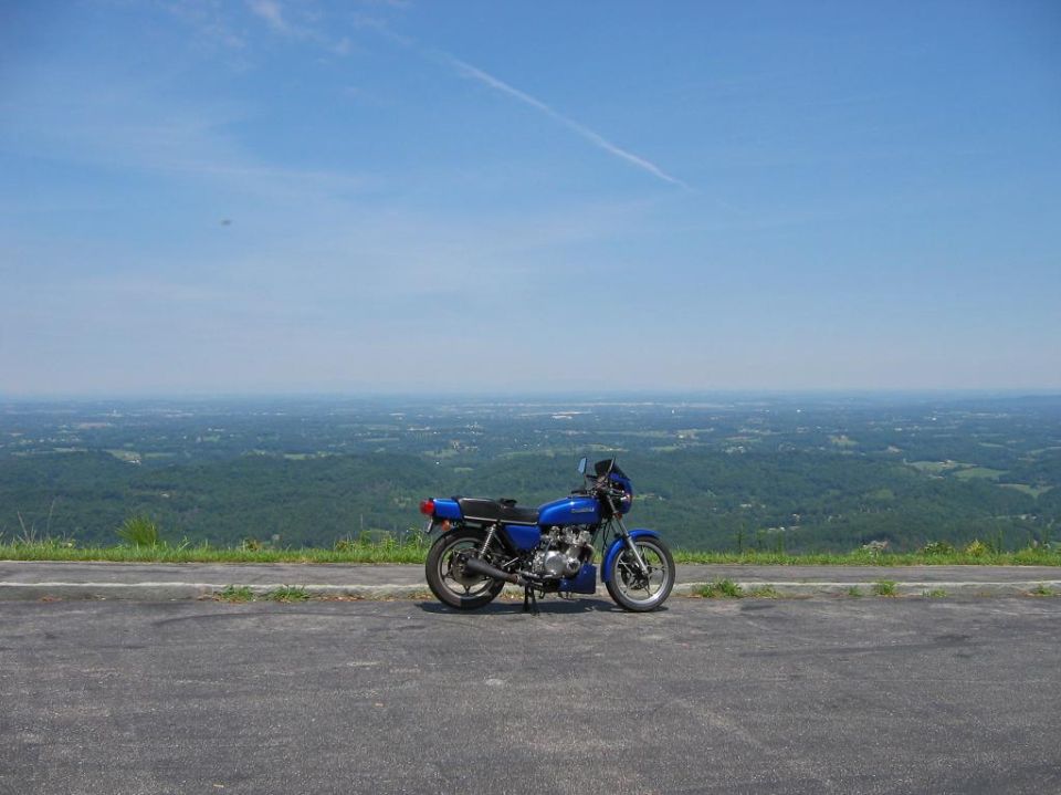 Blue motorcycle parked on asphalt with a scenic overlook in the background