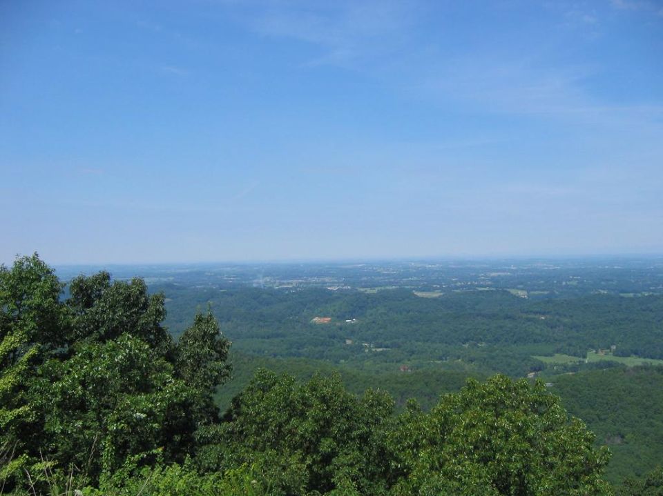 Panoramic view of rolling green hills and distant town under a clear blue sky