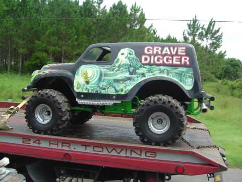 1993 Ford Bronco - A custom monster truck, branded 'Grave Digger', is transported on a tow truck.