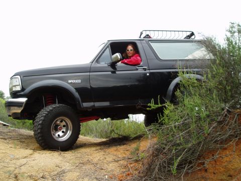 1992 Ford Bronco - A black 1992 Ford Bronco navigates an off-road trail with a driver behind the wheel.