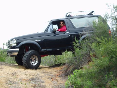 1992 Ford Bronco - A black 1992 Ford Bronco with a lifted suspension navigates an off-road trail.