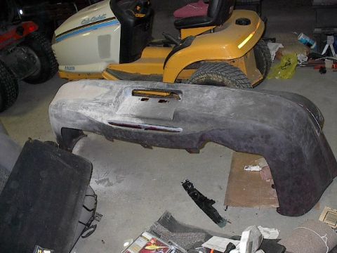 1993 Ford Probe - A car bumper, possibly for a 1993 Ford Probe, sits on the floor surrounded by other parts and lawnmowers.