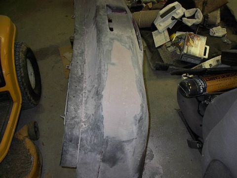 1993 Ford Probe - A car bumper is undergoing repair work, with body filler applied to a damaged area. A yellow lawn tractor is partially visible to the left.
