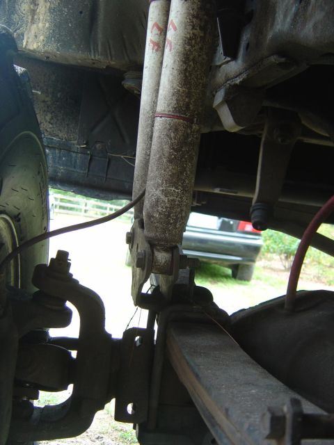 1993 Ford Bronco - Underside view of a truck's rear suspension showing dusty twin shock absorbers with red decals, a leaf spring, axle, brake backing plate an…