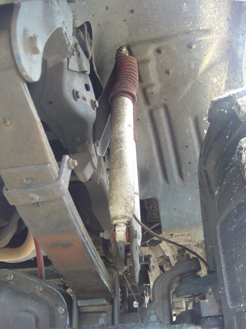 1993 Ford Bronco - Looking up from under a truck at a silver-bodied shock absorber with a weathered red accordion dust boot at its top, mounted between a fram…