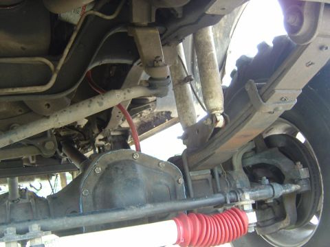 1993 Ford Bronco - Underside view of a vehicle showing the front differential housing, drive components, and suspension parts including a red rubber boot/bell…