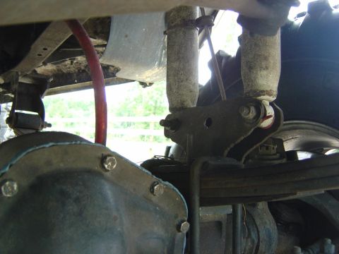 1993 Ford Bronco - Looking up under a truck's rear axle, showing the differential cover with its ring of bolts, a leaf spring and shackle plate, and a red bra…