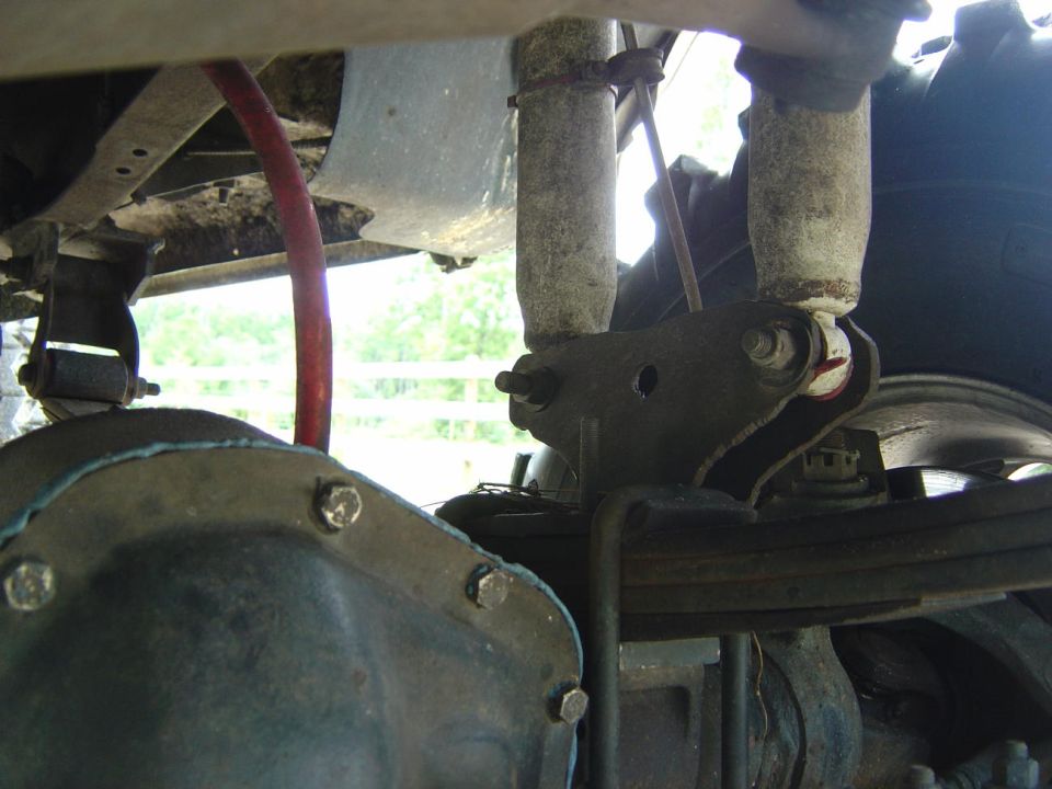 Underbody view of rear differential cover, leaf spring shackle and red brake line