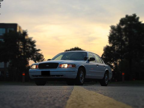 2000 Ford Crown Victoria - A white Ford Crown Victoria is parked on a road as the sun sets, casting a warm glow on the sky.