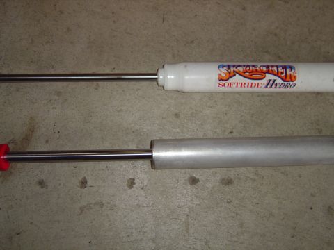 1978 Ford Bronco - Comparison of two shock absorbers, one branded Skyjacker, against a concrete surface.