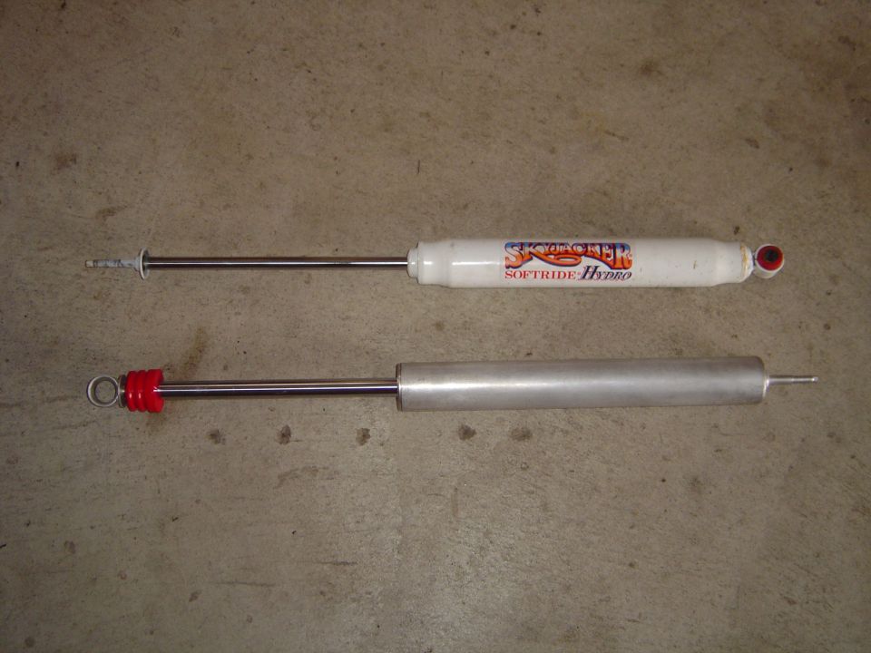 Two shock absorbers, one white with red top, one silver with red top
