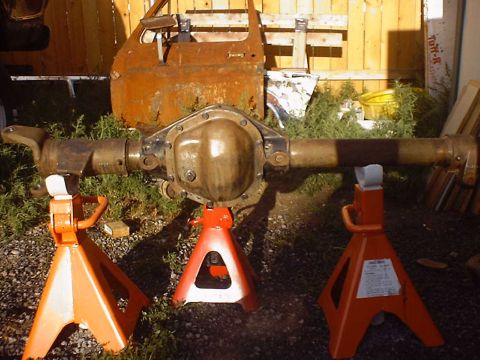 1988 Ford Bronco - Rear axle assembly supported by jack stands, with a rusty car door behind it.