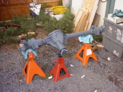 1988 Ford Bronco - Rear axle assembly, primed and painted, rests on jack stands outdoors.
