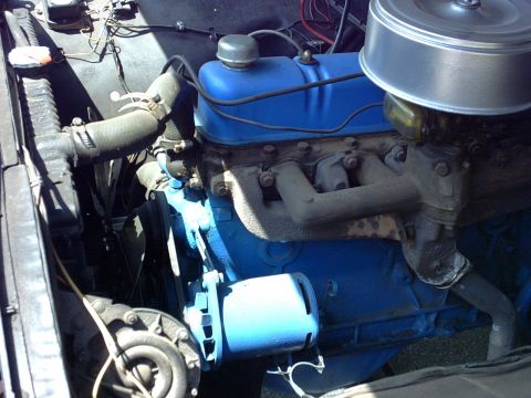 1954 Ford F-100 - The engine bay of a vehicle, showing the motor, hoses, and air filter assembly.