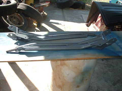 1990 Ford Bronco - Pair of gray suspension components, possibly for a lift kit, resting on a workbench.