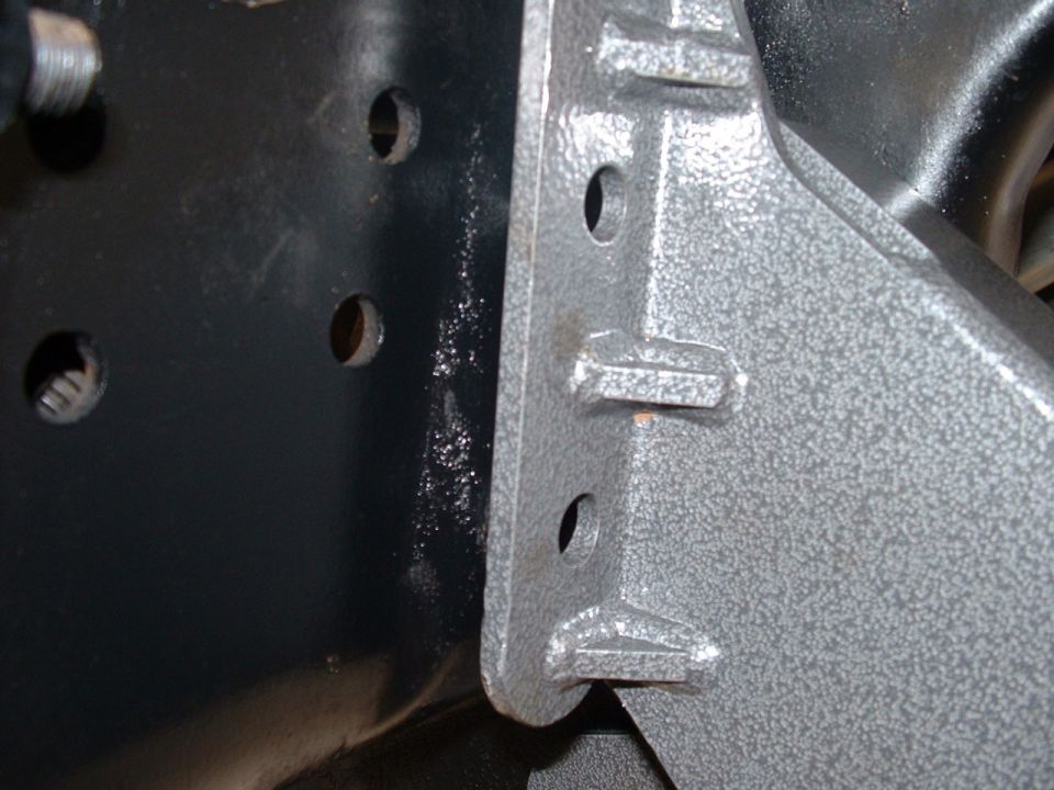 Close-up of a metal bracket bolted to a black frame component, with several holes visible