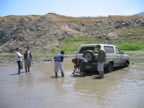 1985 Ford Bronco - A group of people stand around a white Ford Bronco that is stuck in muddy water.