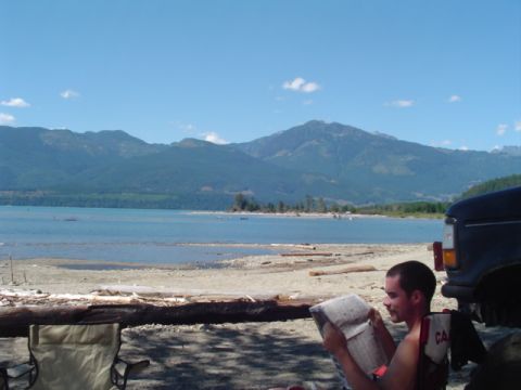 1993 Ford Bronco - A man relaxes by a lake next to a black Ford Bronco, with mountains in the background.