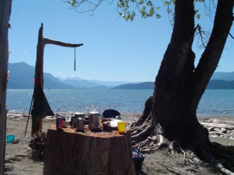 1993 Ford Bronco - A scenic campsite is set up on a beach, cooking equipment on a log table with a lake and mountains in the distance.