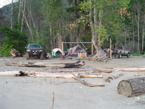 1993 Ford Bronco - A beach campsite is set up with tents and two SUVs parked nearby among driftwood.