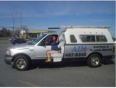 1986 Ford Bronco - A silver pickup truck with a camper shell displays "AIM Electrical & Plumbing Services" and a phone number on its side.