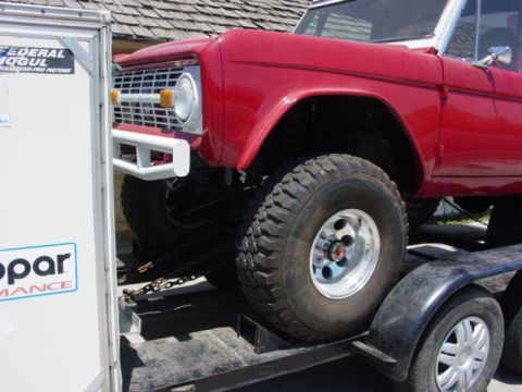 1992 Ford Bronco - A red Ford Bronco is being loaded onto a trailer, showing its front quarter panel and large tires.