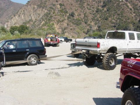 1992 Ford Bronco - Several off-road vehicles are gathered in a sandy area, with one truck towing another.