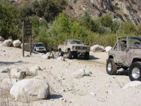 1992 Ford Bronco - A tan pickup truck navigates a rocky, off-road path near a stream crossing sign.