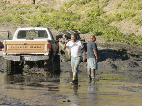 1992 Ford Bronco - Two men stand in muddy water next to a Dodge Ram pickup truck that appears to be stuck.