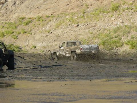 1992 Ford Bronco - A truck churns up mud as it navigates a challenging off-road course, with another vehicle nearby.