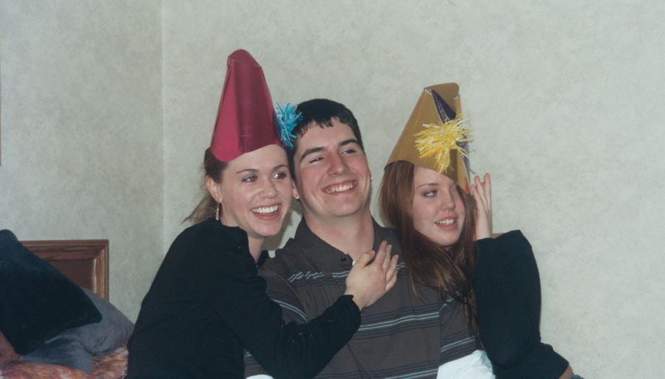 Three people in party hats smiling together indoors; no vehicle shown