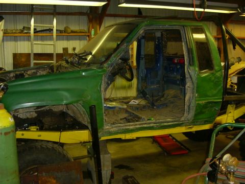1990 Ford Bronco - A green pickup truck chassis sits in a workshop, stripped down and awaiting repairs or modification.