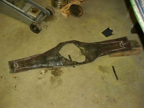 1990 Ford Bronco - A damaged metal part with white markings lies on a concrete floor next to a car jack.