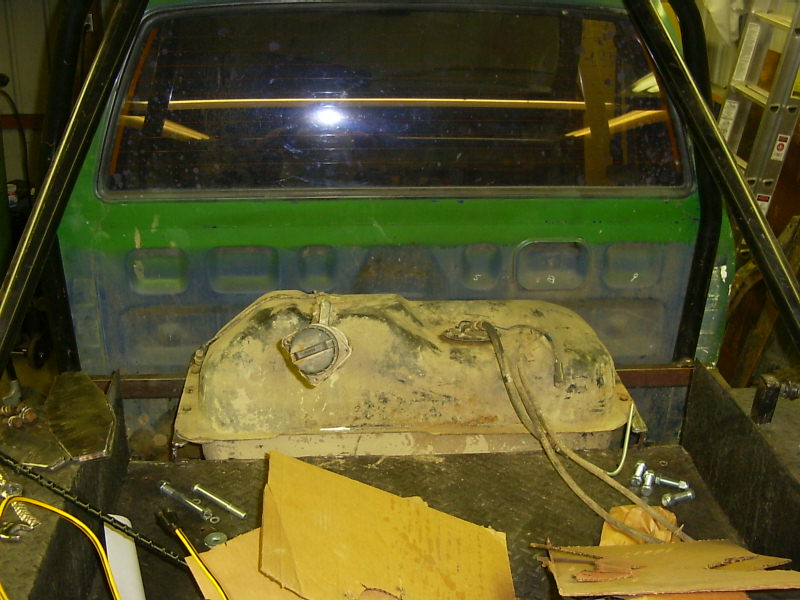 Green truck bed interior with a rusty fuel tank and roll cage. Hardware is scattered
