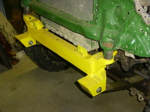 1990 Ford Bronco - Close-up of a yellow bumper bracket attached to the front of a green vehicle, with a tire visible.