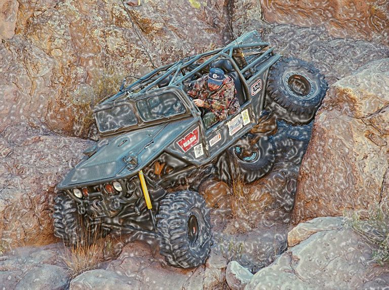 Custom off-road buggy with roll cage climbing a rocky incline. Driver wears camouflage