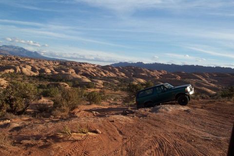 1996 Ford Bronco - A green 1996 Ford Bronco navigates a steep, rocky trail in a desert landscape under a blue sky.