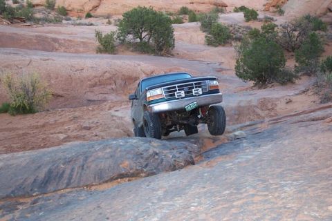 1996 Ford Bronco - A dark green Ford Bronco navigates a rocky off-road trail in a desert landscape.