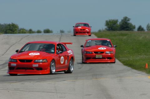 2000 Ford Mustang - Multiple Ford Mustangs compete on a sunny day at a race track.