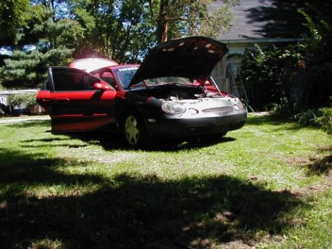 1997 Ford Taurus - A red 1997 Ford Taurus sits in a yard with its hood and driver's side doors open.