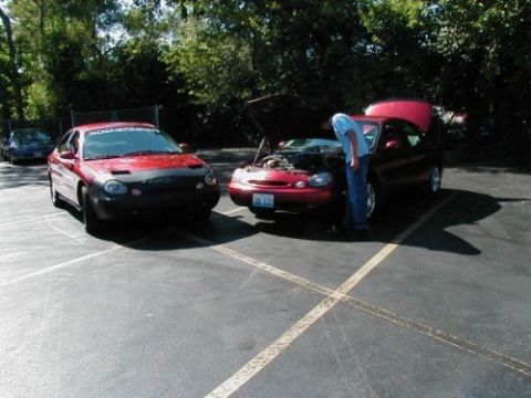 1997 Ford Taurus - Two red Ford Taurus sedans are parked in a lot, one with its hood open as a person inspects the engine.