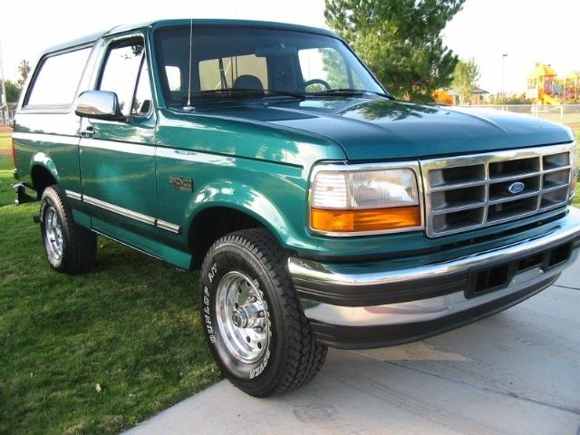 Teal Ford Bronco SUV with white top, 3q-front view on driveway